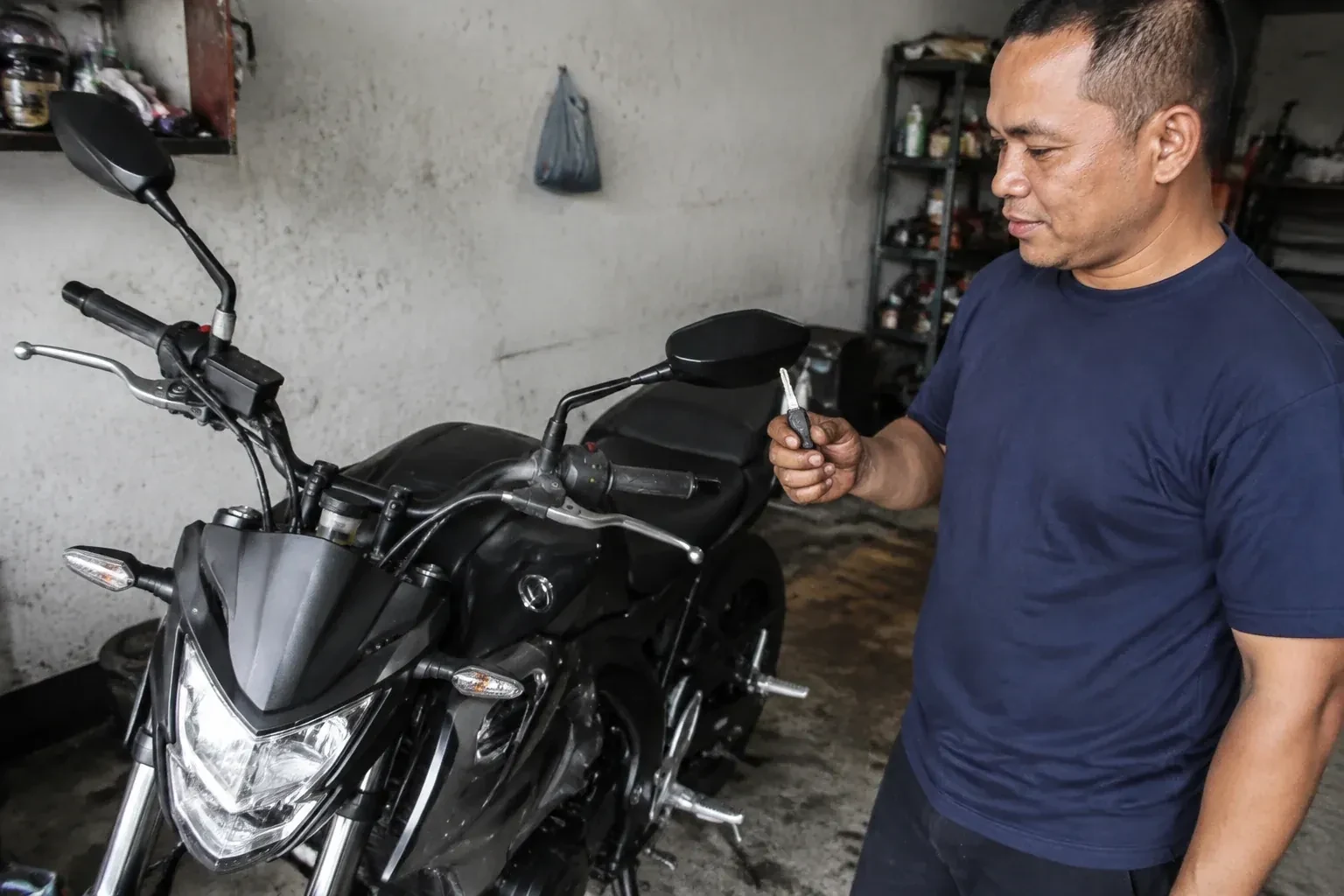 Person holding a key beside a black motorcycle in a garage. — Motorcycle & Scooter Keys, Mississauga